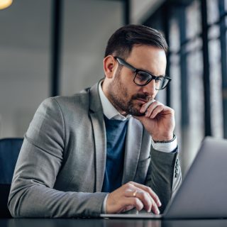 Focused adult man, reading about inflation and the insurance industry on his laptop.