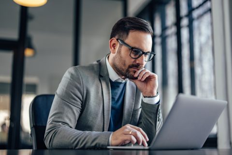 Focused adult man, reading about inflation and the insurance industry on his laptop.