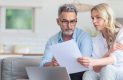 Middle age couple looking at a laptop and paper relating to taxes