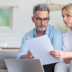 Middle age couple looking at a laptop and paper relating to taxes