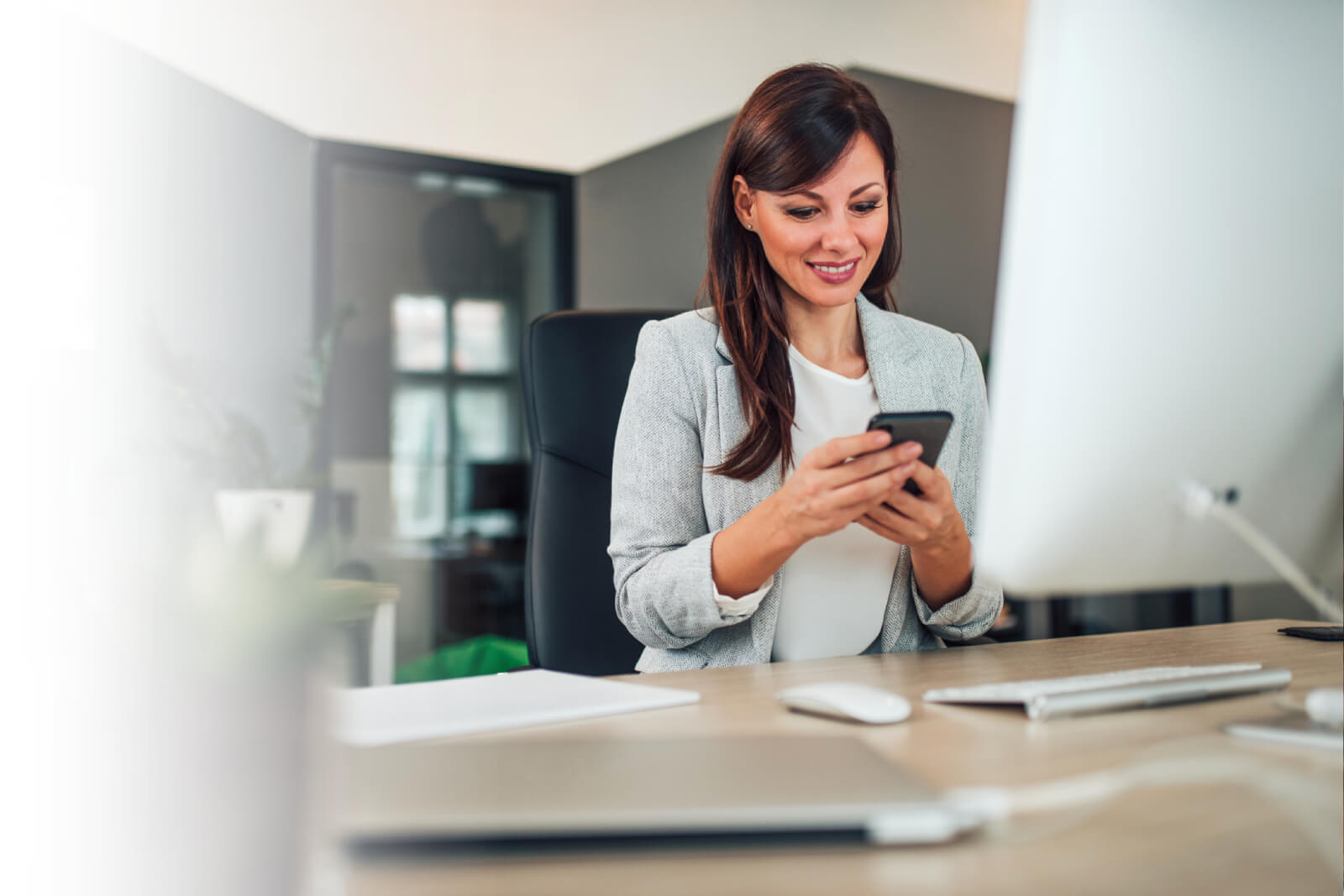 Woman sitting at desktop with phone, researching finances